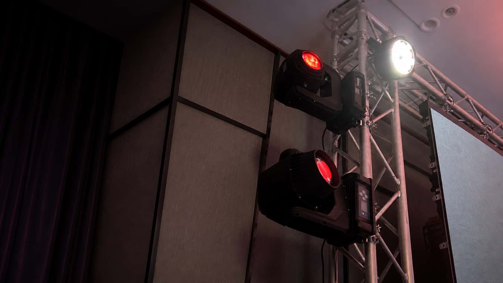 Moving-head lighting fixtures mounted on truss at an indoor event