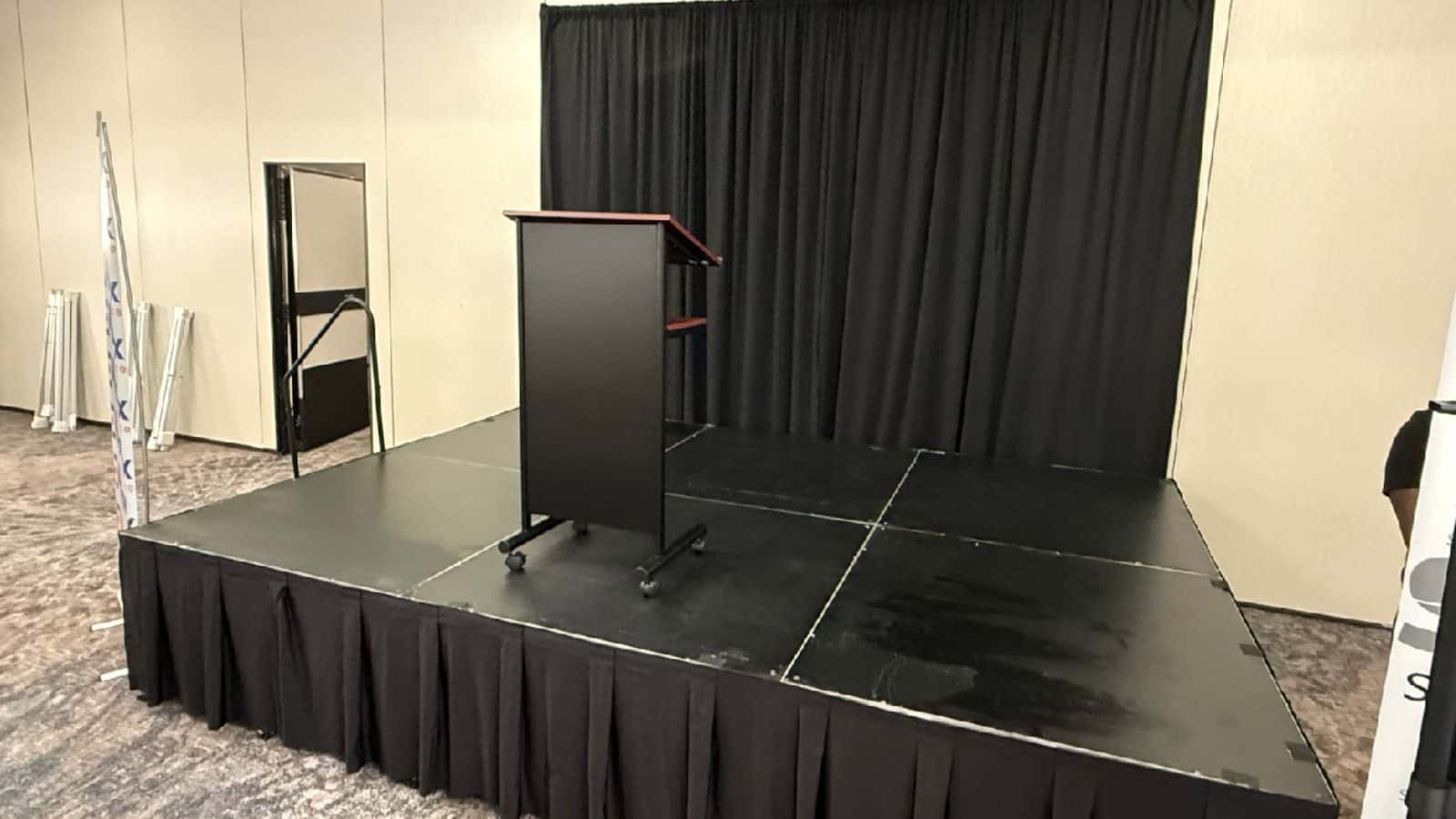 Wheeled lectern positioned on a small presentation stage with black drape