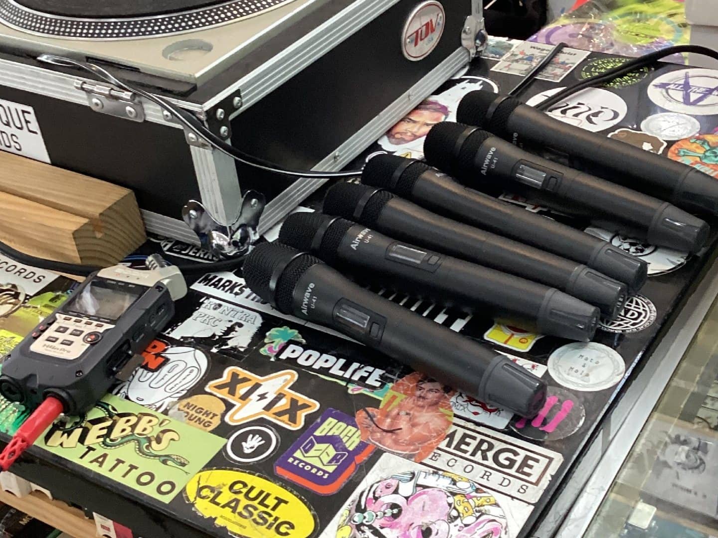 Older handheld field recorder beside wireless microphones on a production case