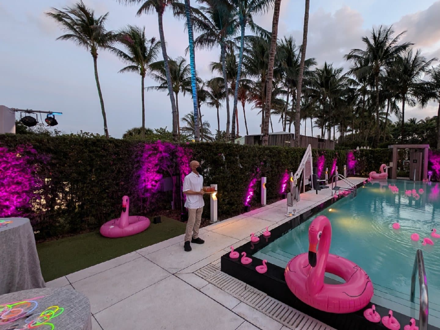 Pink uplights spaced along a hedge beside an outdoor pool event