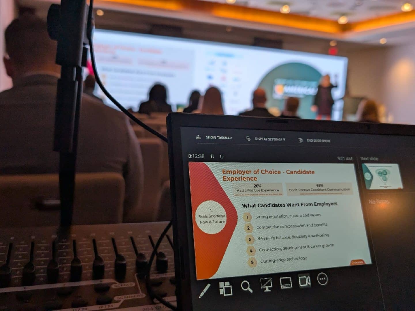 Laptop displaying a presenter view beside a conference projection screen