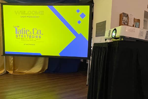 Laser projector positioned beside a projection screen during an event presentation
